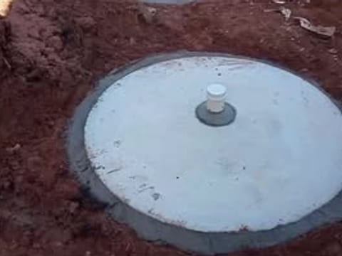 Tampa redonda de concreto de uma fossa recém-instalada, com o respiro no centro