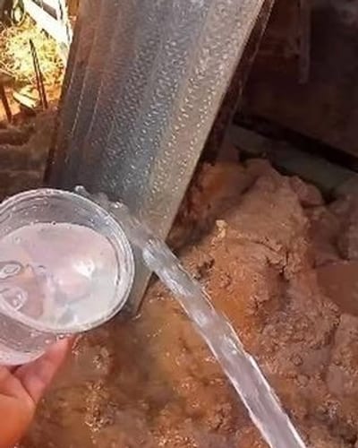 Água limpa saindo do cano de um poço recém-perfurado e enchendo um copo transparente